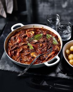 a bowl of stew next to two bowls of potatoes and water on a black table