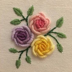 three crocheted flowers with green leaves on a white surface, one is pink and the other is yellow