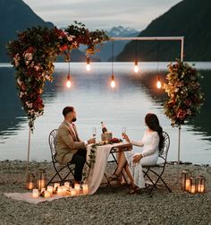 a man and woman sitting at a table next to each other with candles on the ground