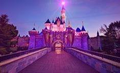 the entrance to disneyland's castle lit up in purple and blue at night time