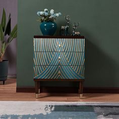 a blue vase sitting on top of a wooden dresser next to a plant and pot