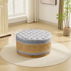 a round ottoman sitting on top of a wooden floor next to a plant in a living room