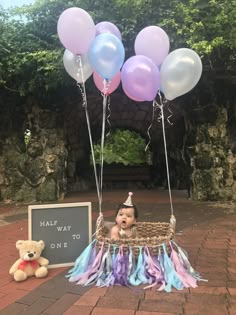 a baby in a basket with balloons and a sign that says may be way to one