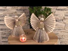 two angel statues made out of old book pages sitting on a table next to a candle