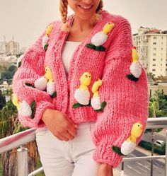 a woman is wearing a pink sweater with yellow ducks on it and white pants, while she has her hands in her pockets