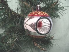 a christmas ornament hanging from a pine tree with red and white designs on it