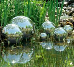 three shiny balls are in the water near some grass and plants on the edge of the pond