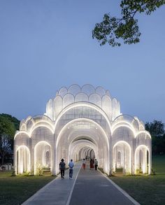 two people walking down a long walkway in front of a white building with lights on it