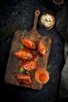 chicken wings with sauce and parsley on a wooden cutting board next to a jar of dipping sauce