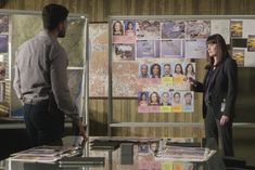 a man and woman standing in front of a bulletin board with pictures on the wall