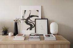 a wooden table topped with books and vases next to a wall mounted art piece