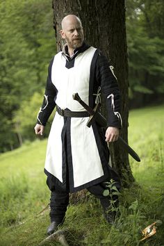 a man dressed as a knight standing next to a tree with two swords in his hands