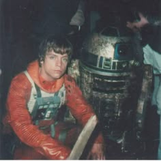 a man in an orange shirt next to a dalen star wars droid costume