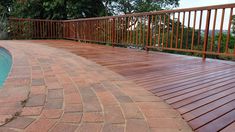 a wooden deck next to a swimming pool in a backyard with brick pavers around it