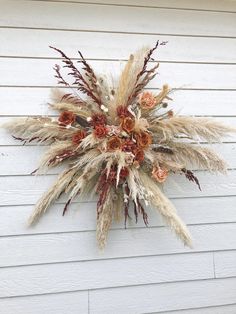 a dried flower arrangement hanging on the side of a white house with red and orange flowers