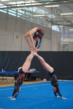 two men doing acrobatic tricks on a blue floor in an indoor gym