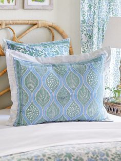 a bed with blue and green pillows on it's headboard next to a wicker chair