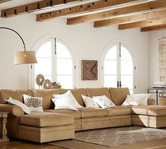 a living room filled with lots of furniture next to two large windows and wooden beams