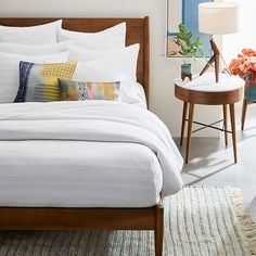 a bed with white sheets and pillows on top of it next to a table with flowers