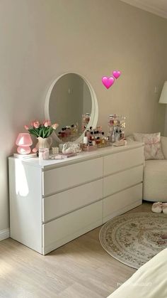 a white dresser sitting next to a bed in a bedroom under a pink heart shaped mirror