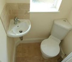 a white toilet sitting next to a sink in a bathroom under a window on top of a tiled floor