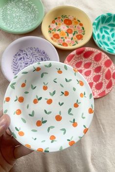 a hand holding a colorful bowl in front of five bowls on a white tablecloth