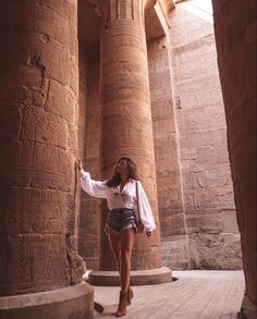 a woman standing in front of an ancient building with her hand up to the ceiling