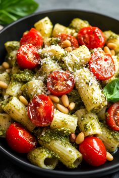 a black bowl filled with pasta, tomatoes and pesto on top of a table