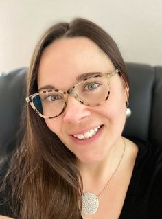 a woman wearing glasses sitting in a chair smiling at the camera with her eyes closed