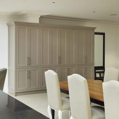 a dining room table with white chairs next to a large cabinet in the middle of it