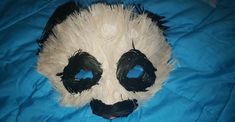 a panda bear mask with black and white feathers on it's face, laying on a blue blanket