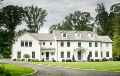 a large white house sitting in the middle of a lush green field next to a road