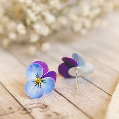 two small blue and purple flowers sitting on top of a wooden table next to white flowers