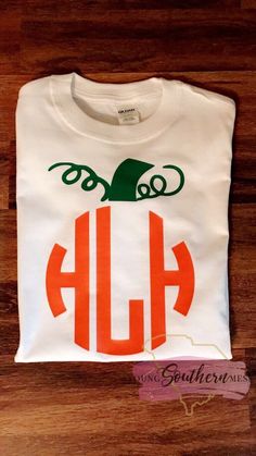 a white shirt with an orange and green monogrammed pumpkin on the front, sitting on a wooden surface