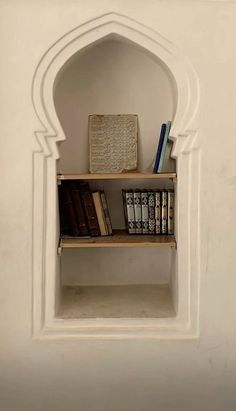 a book shelf with books on top of it and an arch in the wall behind it