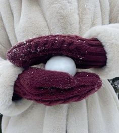 a person wearing a white coat and red mittens holding a snowball in their hand