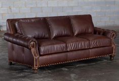 a brown leather couch sitting on top of a cement floor next to a brick wall