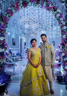 a man and woman standing in front of a floral archway