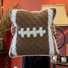 a person holding a crocheted pillow with a football pattern on the front and side