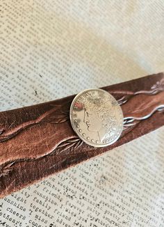 a silver coin sitting on top of a brown leather belt that is laying on an old book