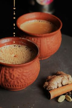 two orange bowls filled with liquid next to some ginger and anise on a table