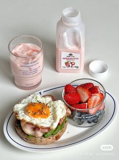 a plate with a sandwich, strawberries and yogurt next to a jug of water