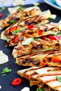 several quesadillas are lined up on a black plate with cheese and peppers