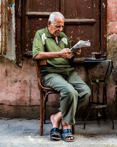 an old man sitting in a chair reading a newspaper