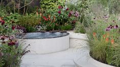 a garden filled with lots of flowers and plants next to a large white tub in the middle