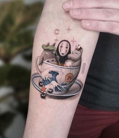 a woman with a tattoo on her arm is holding a cup filled with cats and fish