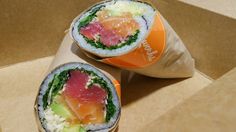 two sushi rolls sitting on top of a brown paper bag next to an orange cup