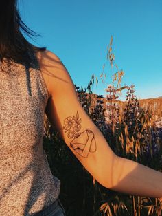 a woman with a tattoo on her arm holding a flower in front of some tall grass