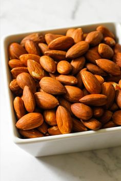 almonds in a square bowl with text overlay that reads oven roasted almonds