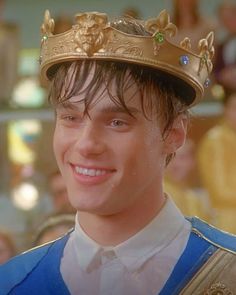 a young man wearing a gold crown and blue vest smiles at the camera while standing in front of an audience